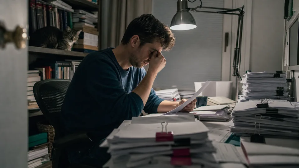 Analityk wieczorem przegląda stos wydruków z rejestrów i sprawozdań